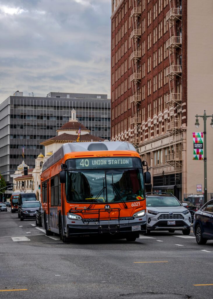 Orange Metro bus navigating downtown Los Angeles near Union Station on a cloudy day.