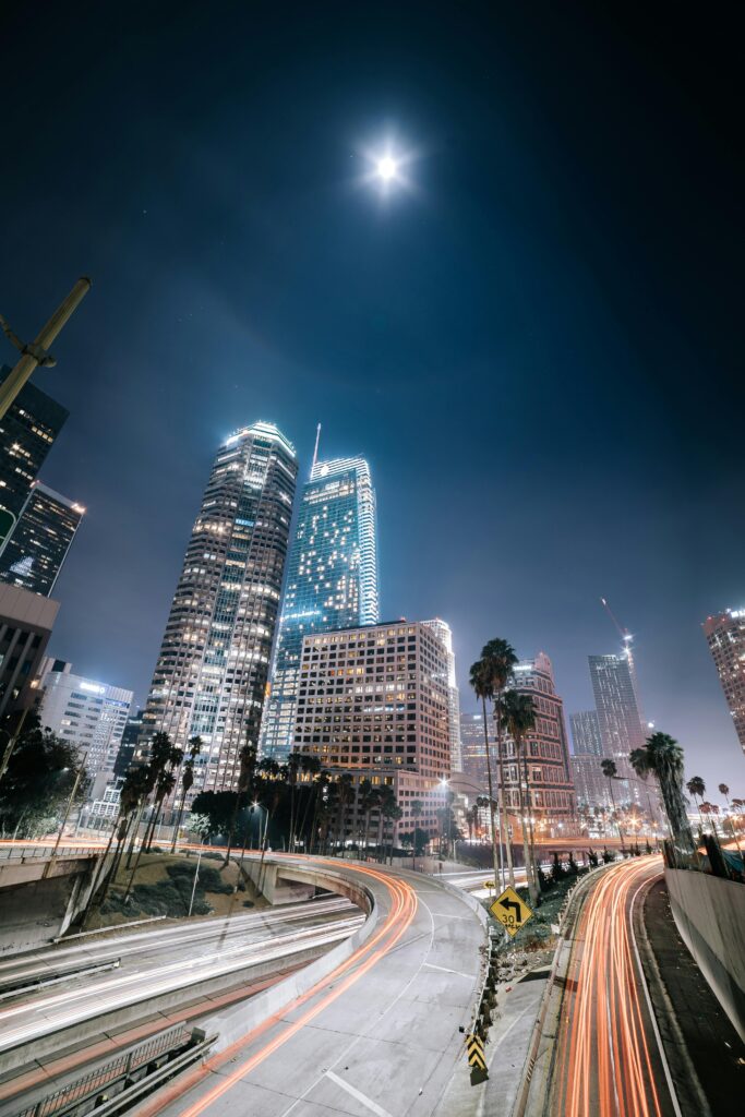 Long exposure of Los Angeles with skyscrapers and light trails under a full moon, capturing urban nightlife.