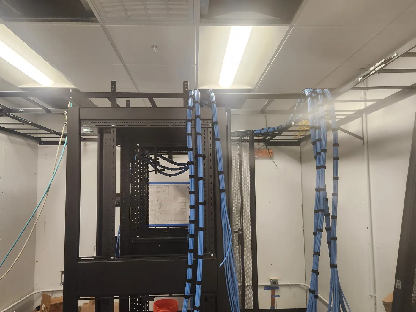 Telecom room mid-install with cable bundles dressed into a new rack and drawings taped to the wall
