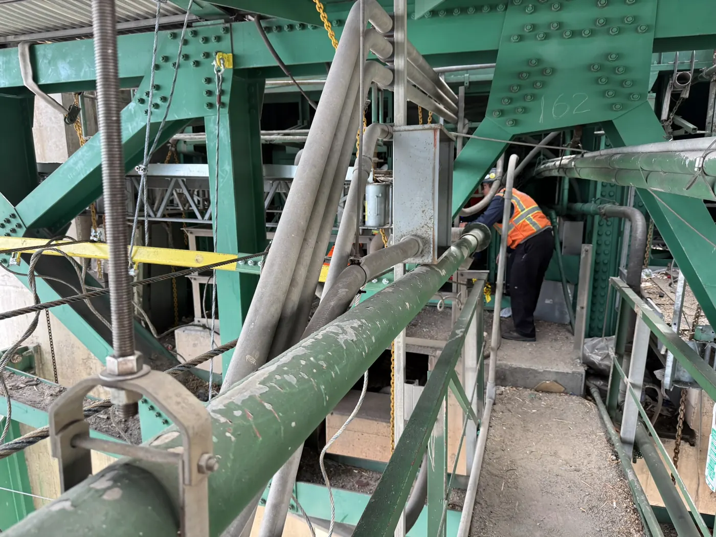 Technician on the maintenance walkway under the bridge deck with conduit runs along the steel